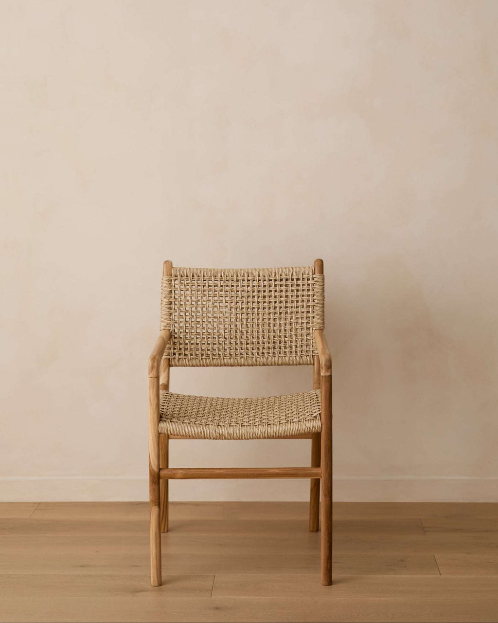 A Marin woven armchair with a natural light wood frame and woven cane backrest and seat, set against a minimalist beige plaster wall and light wood floor.
