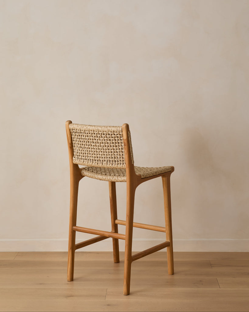 Marin Faux Rattan Counter Stool on white oak floor against beige lime washed wall, back angle view.
