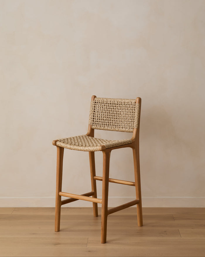 Marin Faux Rattan Counter Stool on white oak floor against beige lime washed wall. Saffron + Poe