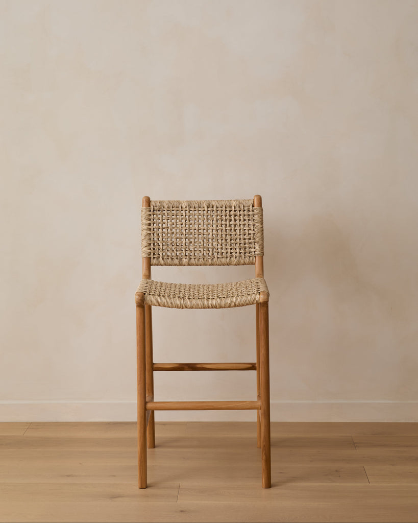 Marin Faux Rattan Counter Stool on white oak floor against beige lime washed wall, front view.