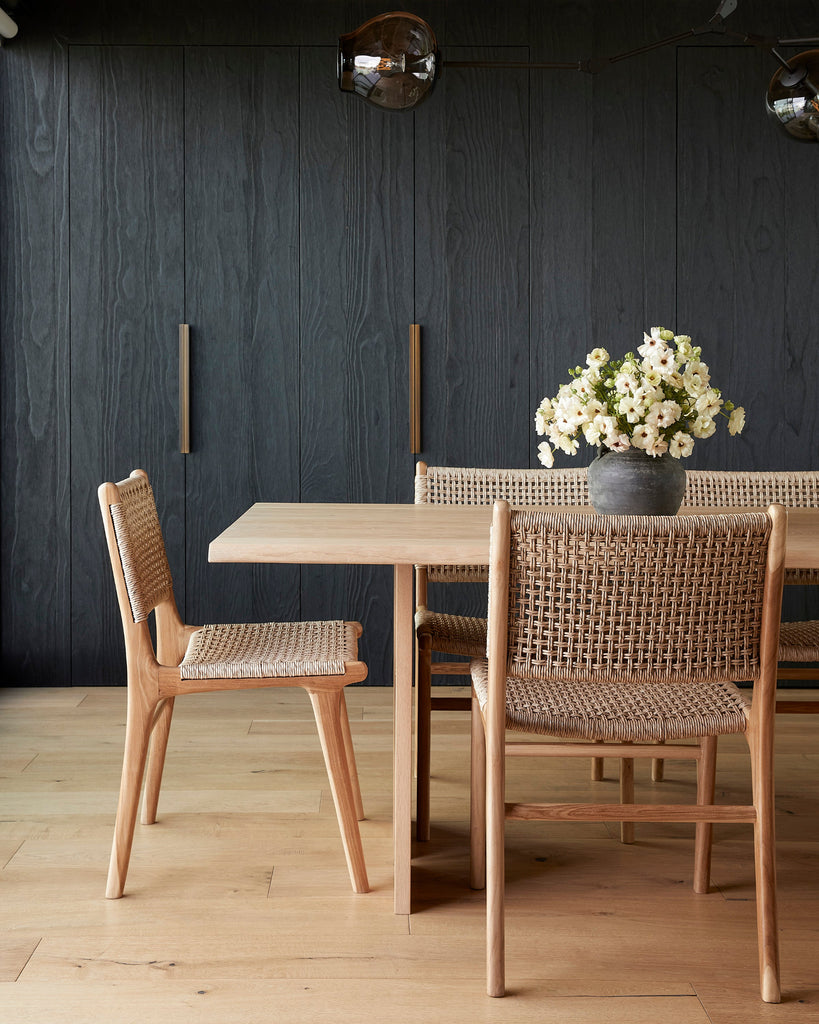 Dining room with wooden table and faux-rattan Marin dining chairs, vase with flowers on the table.