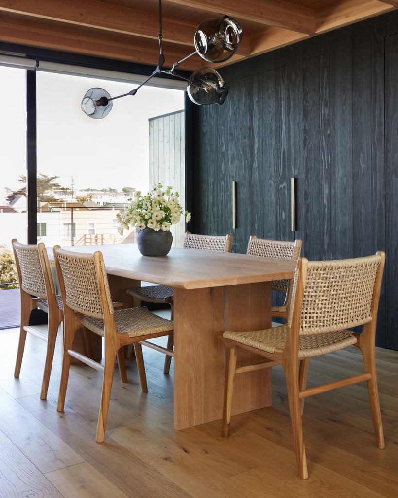 Dining room with wooden table and faux-rattan Marin dining chairs, vase with flowers on the table.
