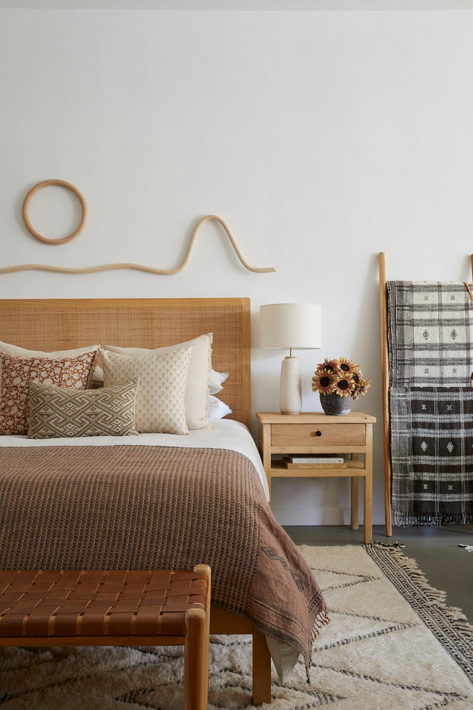 Katie Gong Wood Sculpture Art shot in bedroom above rattan headboard  and woven leather bench. Saffron + Poe, Katie Gong