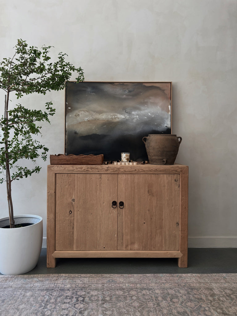 Wooden cabinet with decorative items and an abstract painting against a limewash wall