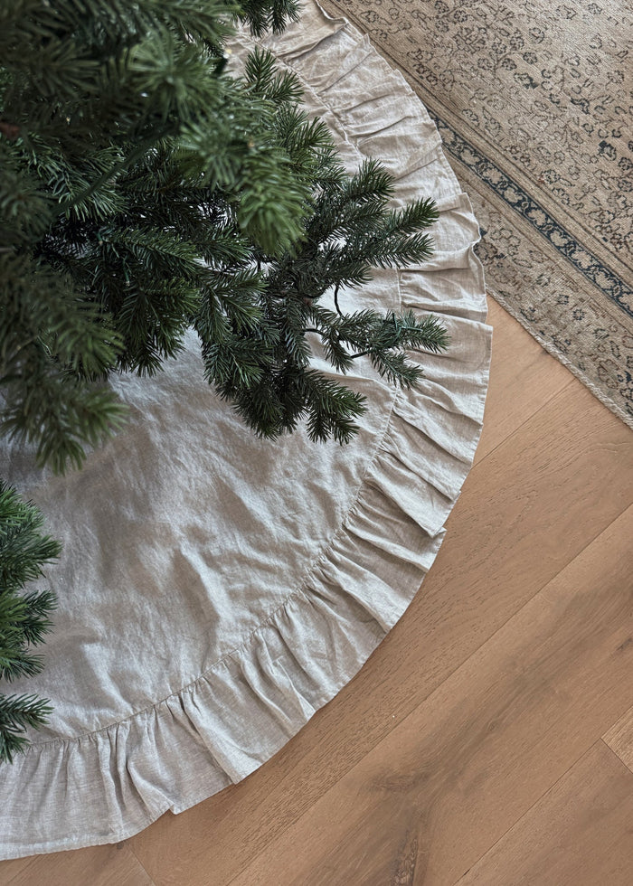 Natural linen ruffled tree skirt with a Christmas tree on a wooden floor.