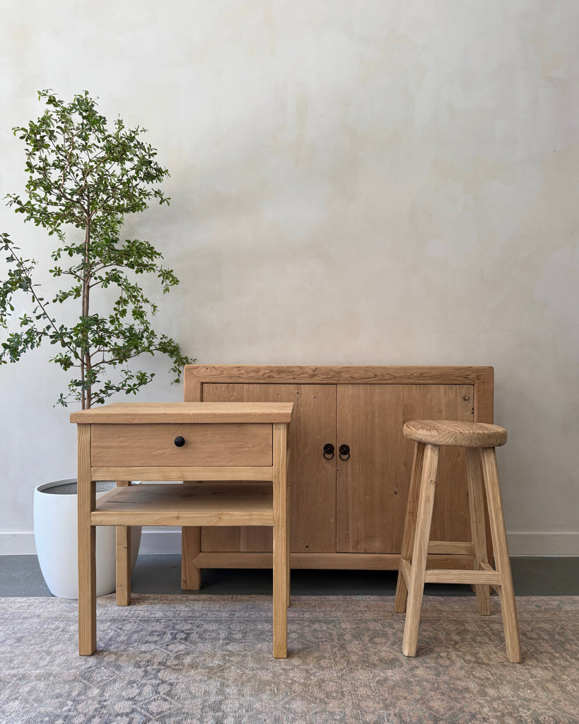Vintage elmwood furniture including a side table, cabinet, and stool in a room with a black olive tree.