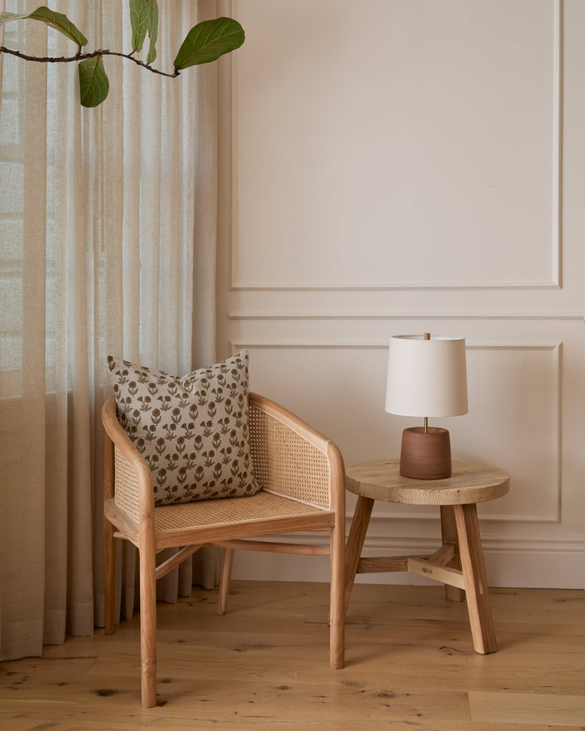 Olivia Rattan Accent Chair Styled in a corner with a side table, blockprint pillow and lamp. Saffron + Poe