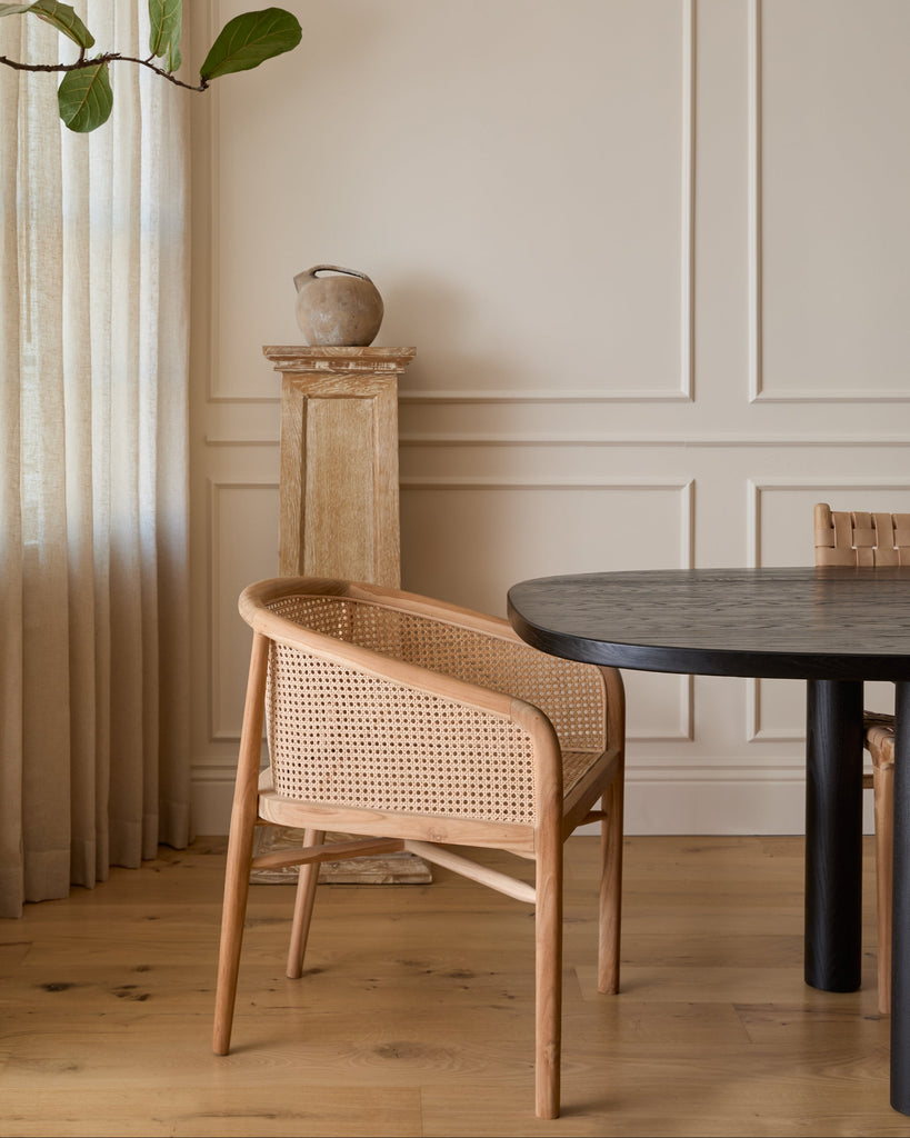 Olivia Rattan Accent Chair styled in a dining room with white oak floors at a black dining table. Saffron + Poe