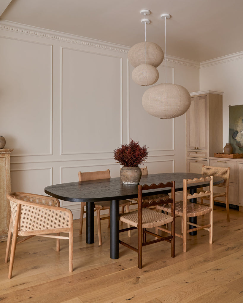 Dining room with a black table and Olivia Rattan Lounge chair, ionian scalloped dining chair, and aegean scalloped dining chair,  featuring a vase of flowers on the table. Saffron + Poe