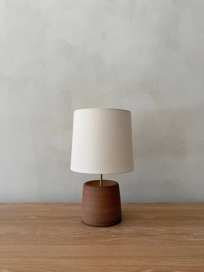 Ostuni Ceramic Table Lamp in Terracotta with oatmeal linen shade on a white oak table against a limewashed wall. - Saffron + Poe