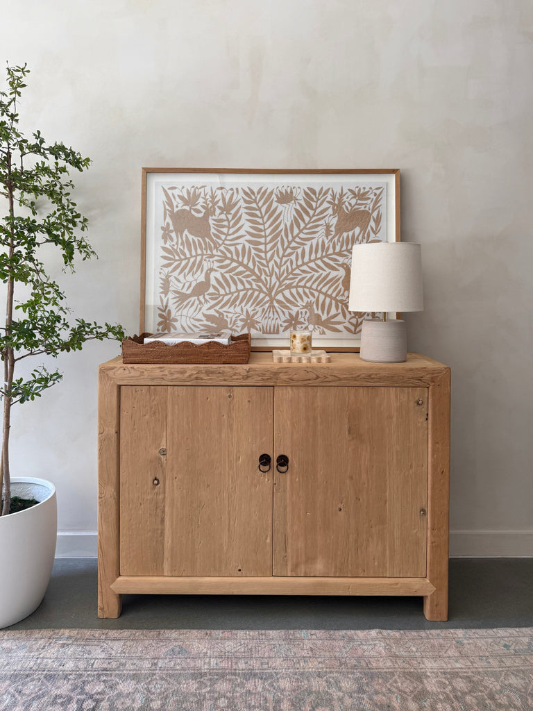 Ostuni Ceramic Table Lamp in Ivory with oatmeal linen shade on a vintage wooden cabinet styled with decorative items. - Saffron + Poe