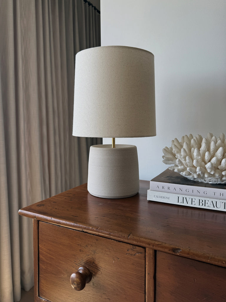 Ostuni Ceramic Table Lamp in Ivory with oatmeal linen shade on a wooden antique dresser with decorative items. - Saffron + Poe