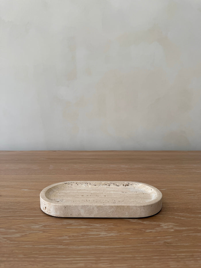 Oval travertine stone tray on a wooden surface with a plain background