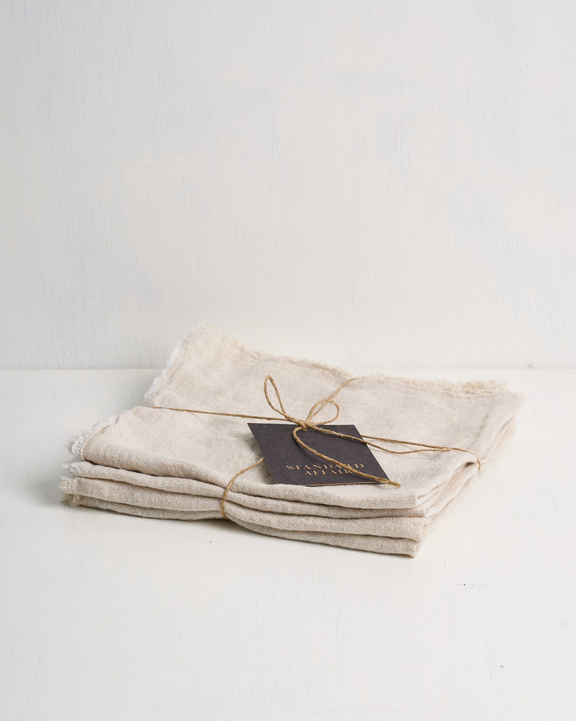 Set of folded beige Philo linen napkins tied with twine on a white surface