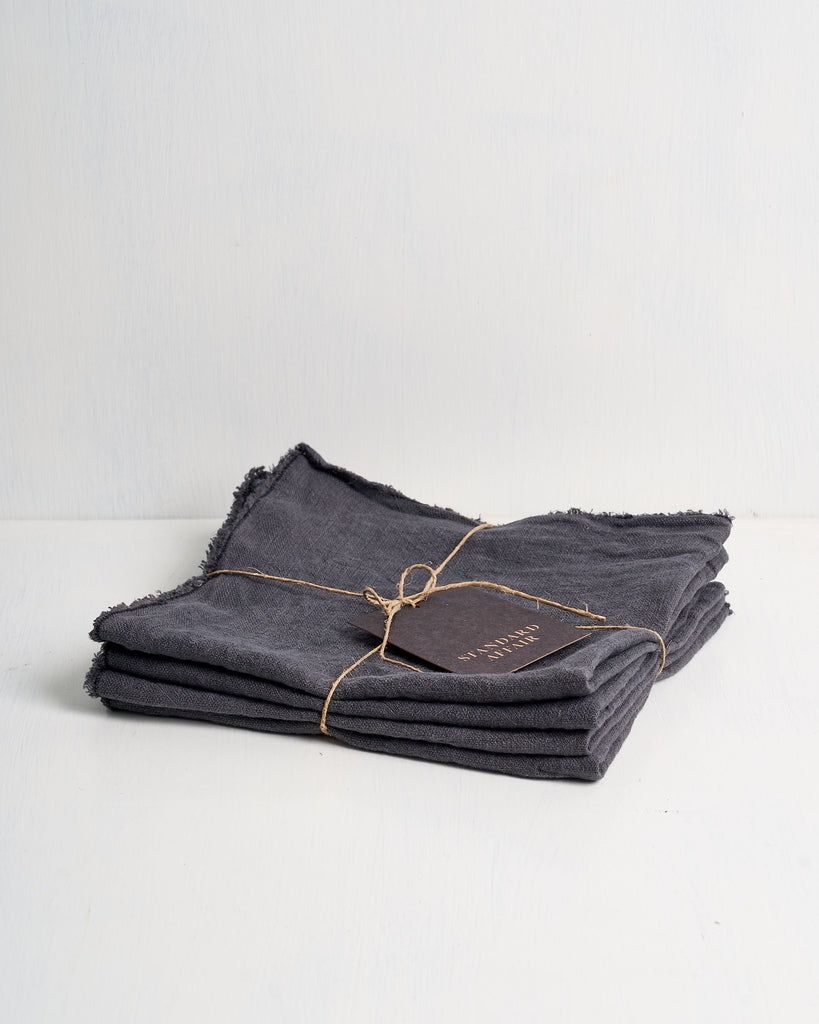 Set of folded slate Philo Linen napkins tied with twine on a white surface