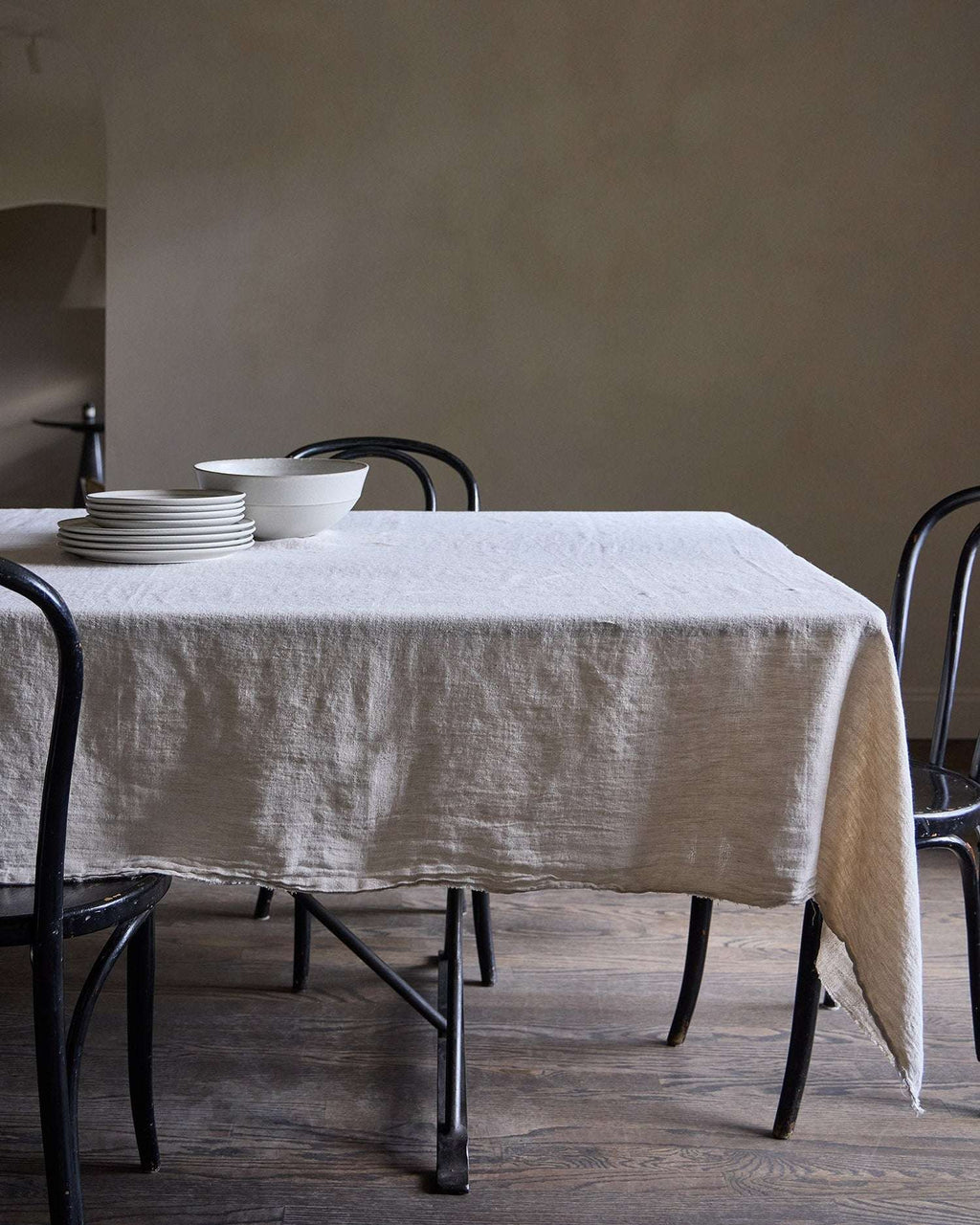 Dining table with a natural Philo linen tablecloth and black chairs against a plain wall.