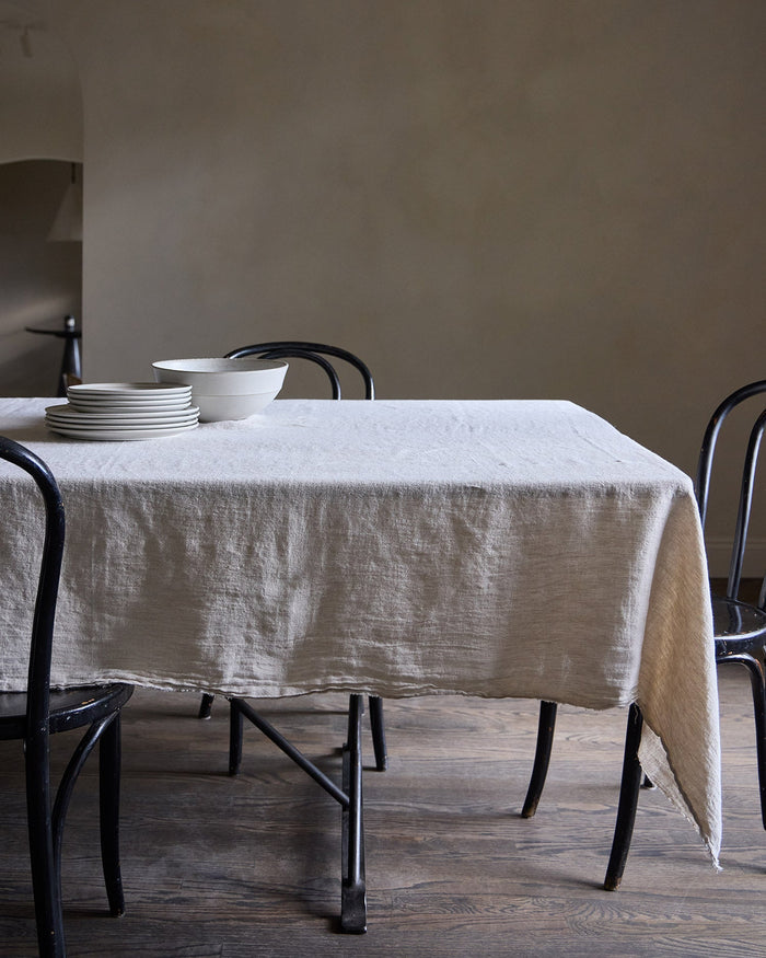 Dining table with a natural Philo linen tablecloth and black chairs against a plain wall.