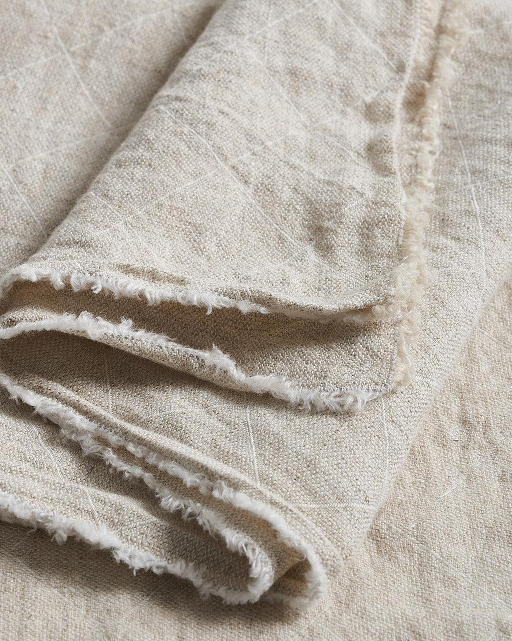 Close-up of beige Philo Tablecloth with frayed edges on a matching background