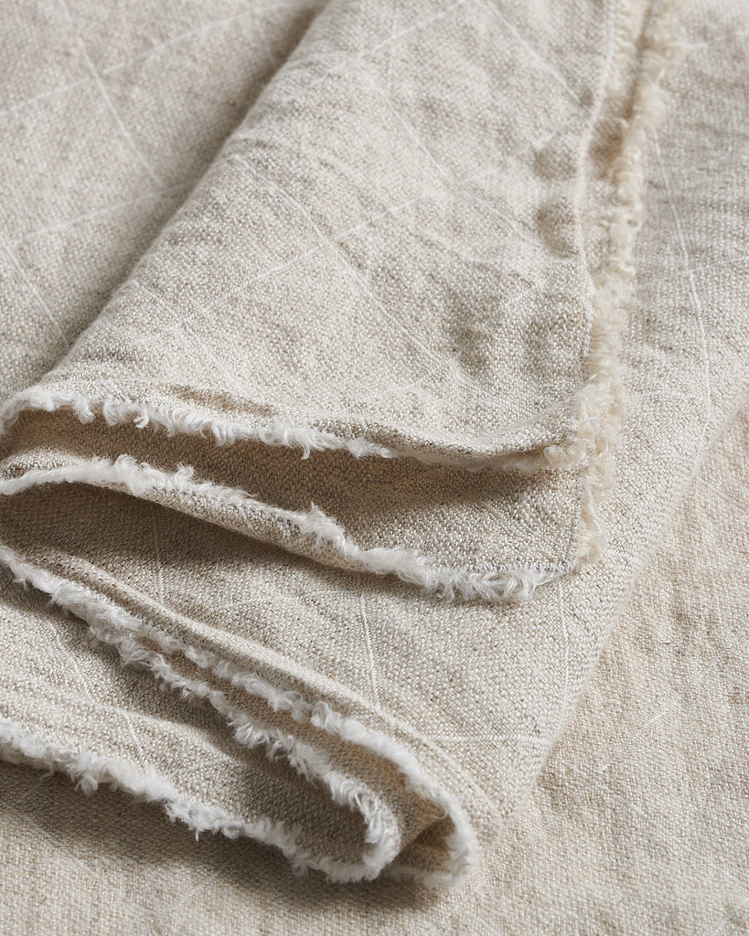Close-up of beige Philo Tablecloth with frayed edges on a matching background