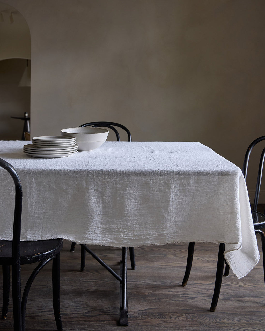 Dining table with a white Philo Linen tablecloth and plates against a plain wall.