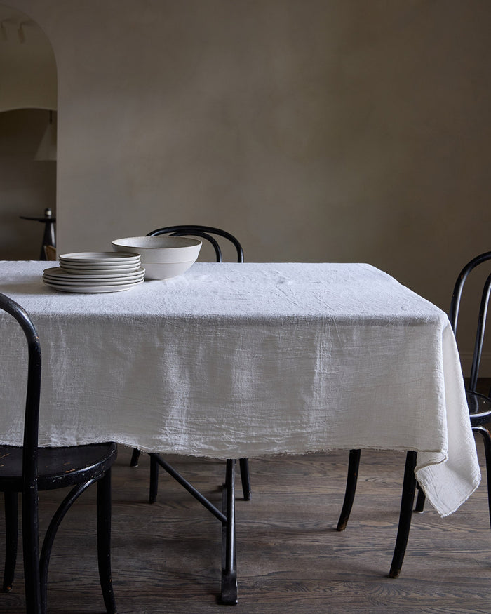 Dining table with a white Philo Linen tablecloth and plates against a plain wall.