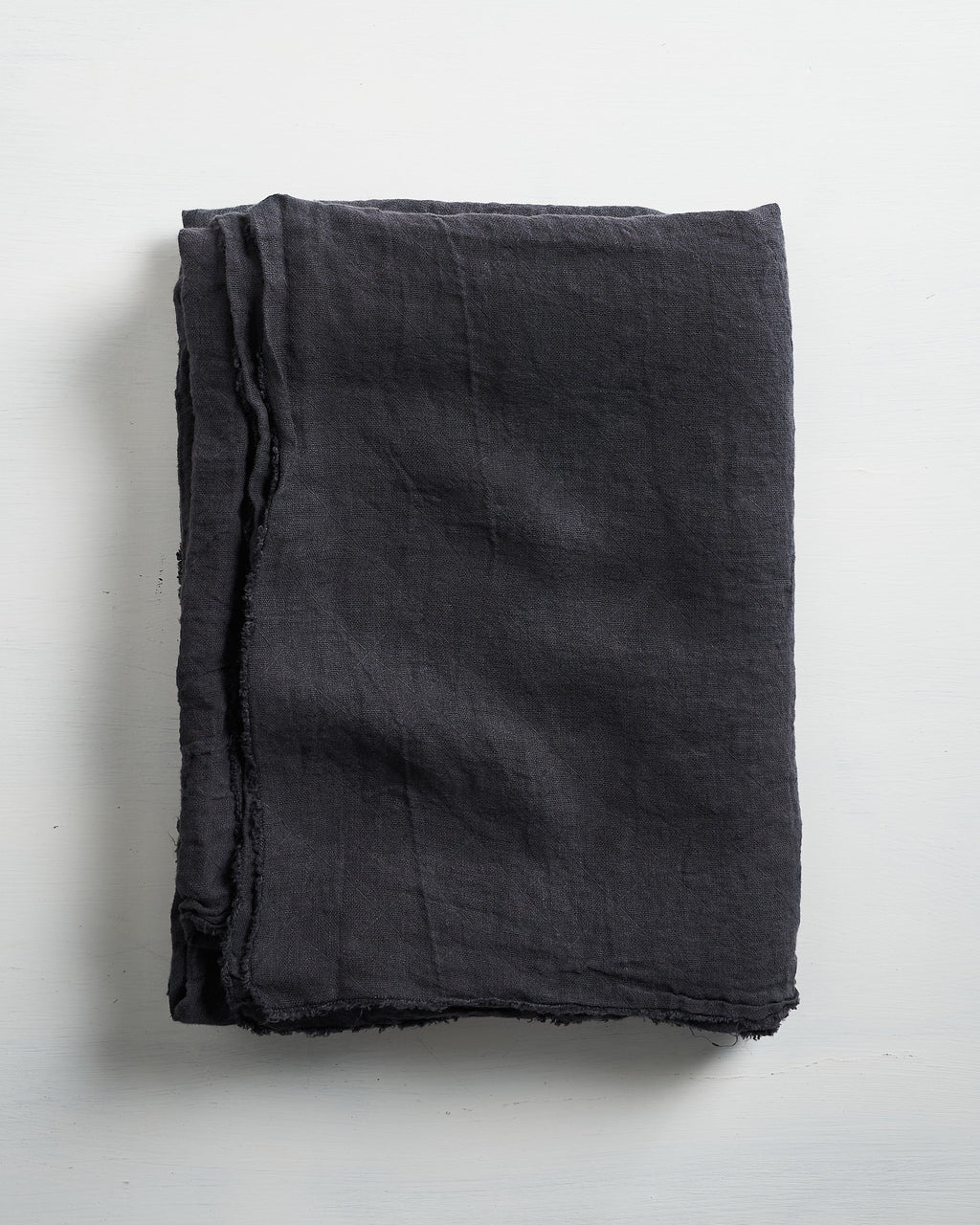 Folded slate Philo linen tablecloth on a light gray background