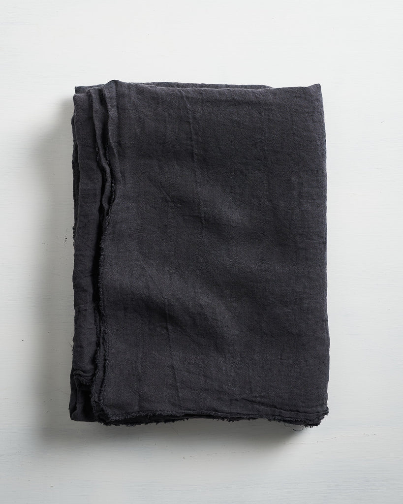Folded slate Philo linen tablecloth on a light gray background