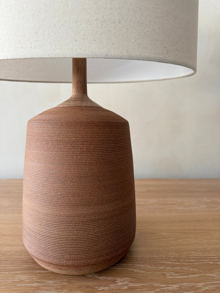 Pienza Ceramic Table Lamp in Terracotta with oatmeal linen shade close up shot on a white oak table against a limewashed wall. - Saffron + Poe