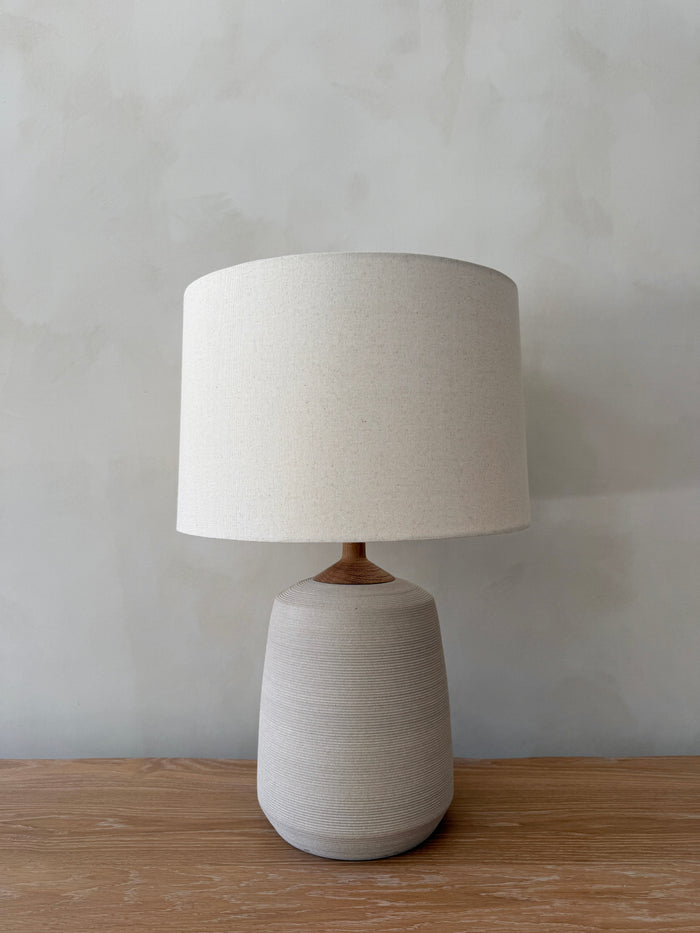 Pienza Ceramic Table Lamp in Ivory with oatmeal linen shade on a white oak table against a limewashed wall. - Saffron + Poe