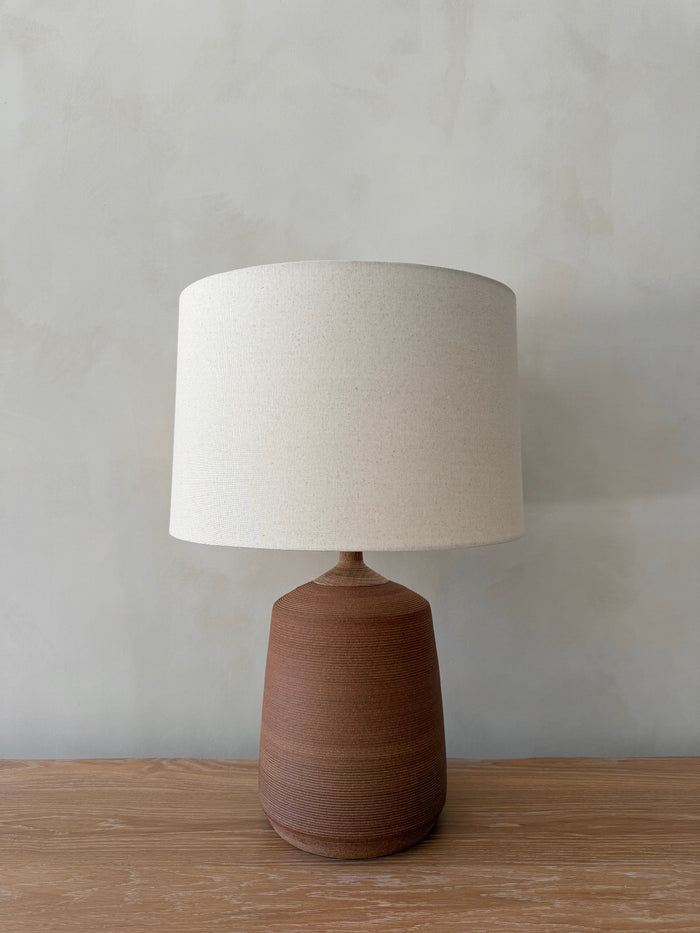 Pienza Ceramic Table Lamp in Terracotta with oatmeal linen shade on a white oak table against a limewashed wall. - Saffron + Poe