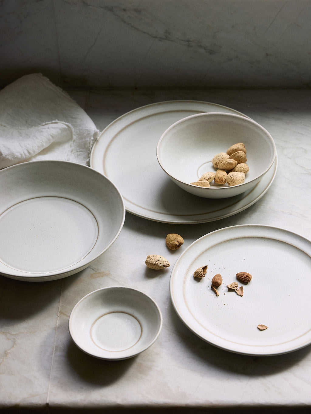 Set of ceramic Pillar plates and bowls on a stone surface with scattered nuts.