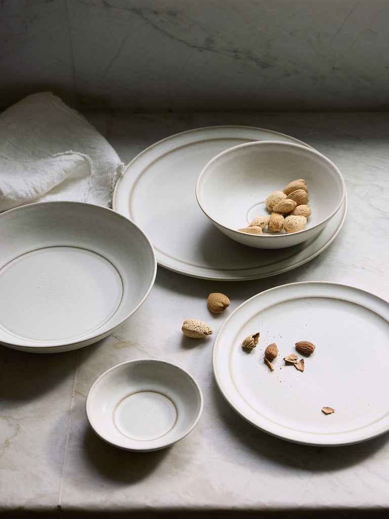 Set of ceramic Pillar plates and bowls on a stone surface with scattered nuts.
