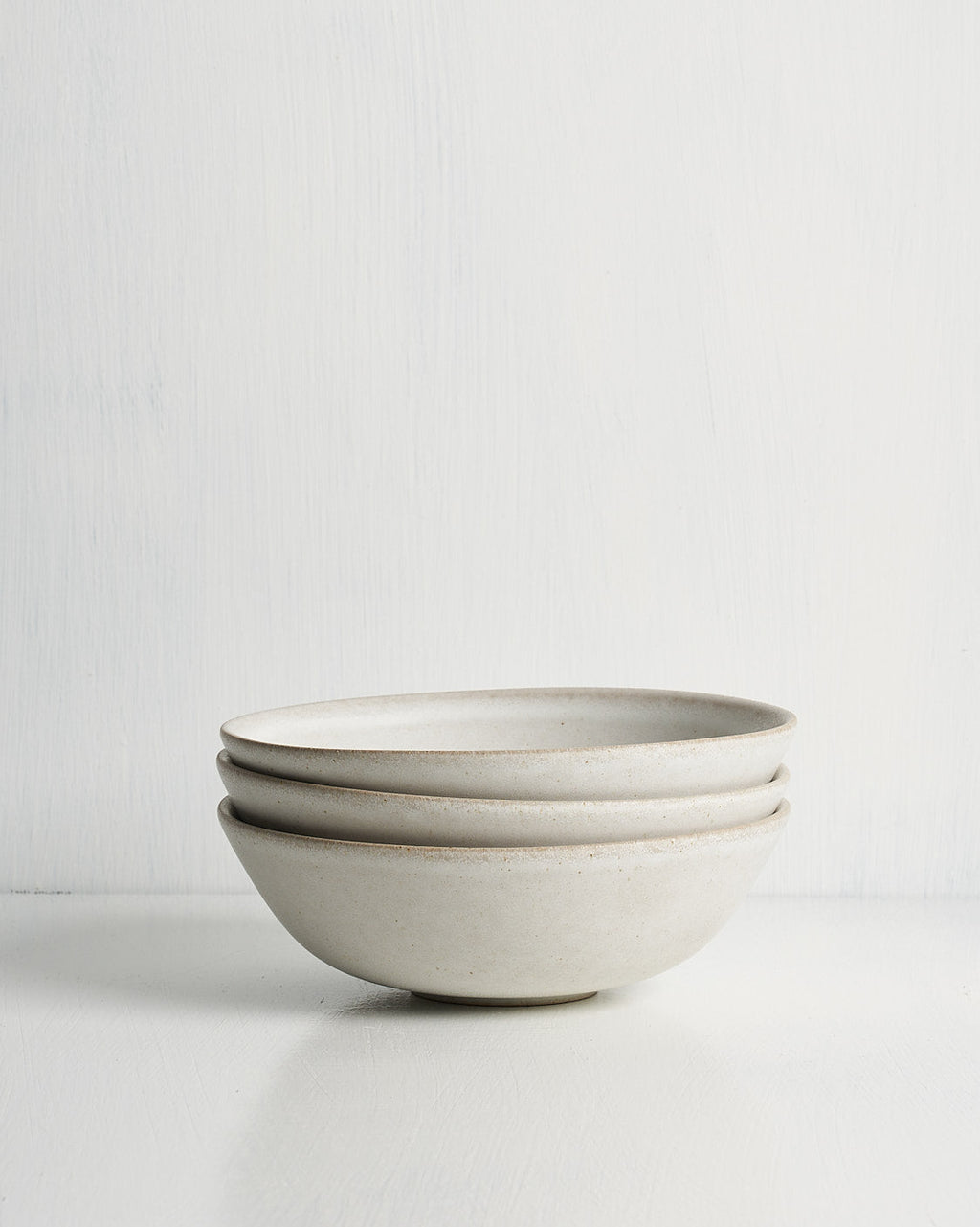 Set of three ceramic low small bowls stacked on a light gray background