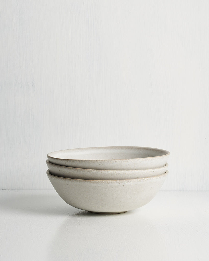 Set of three ceramic low small bowls stacked on a light gray background