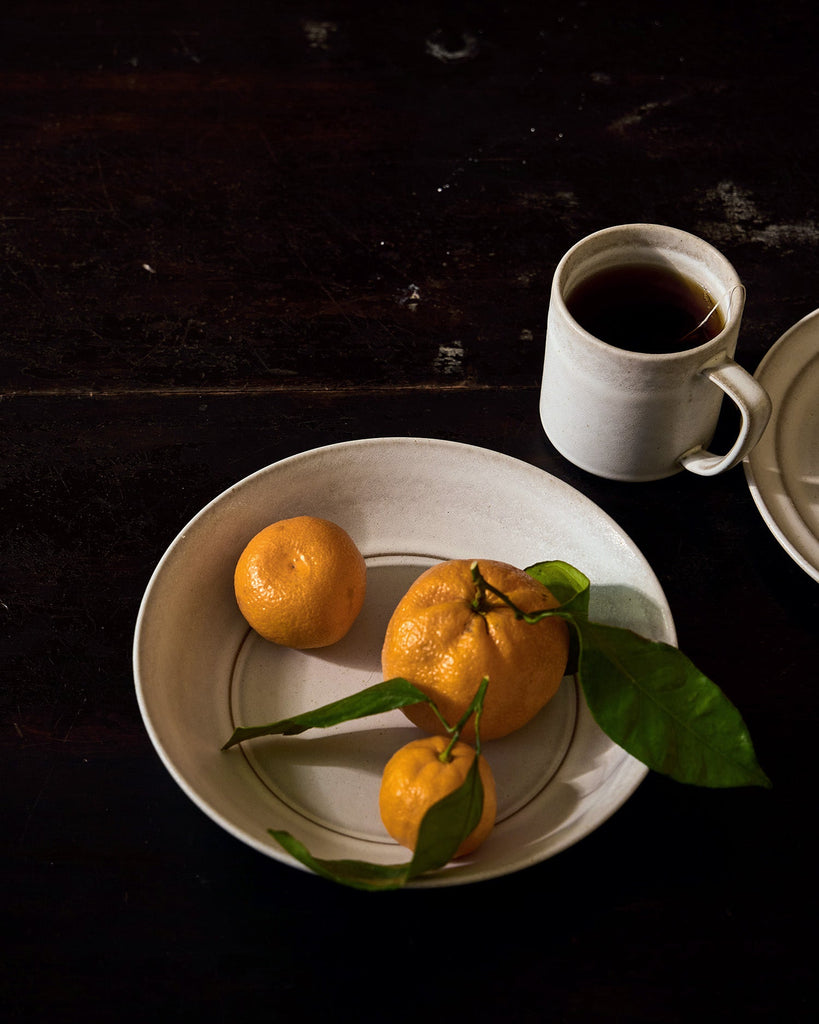 Oranges on a white plate with a Ceramic Pillar mug of coffee on a dark surface