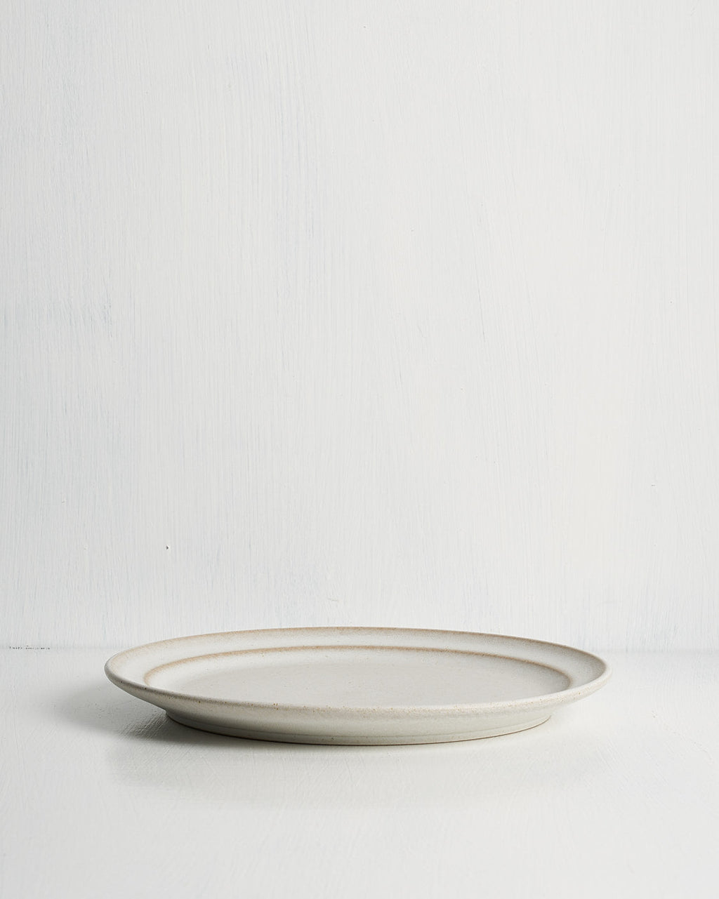 White ceramic pillar salad plate with a thin brown rim on a light gray background