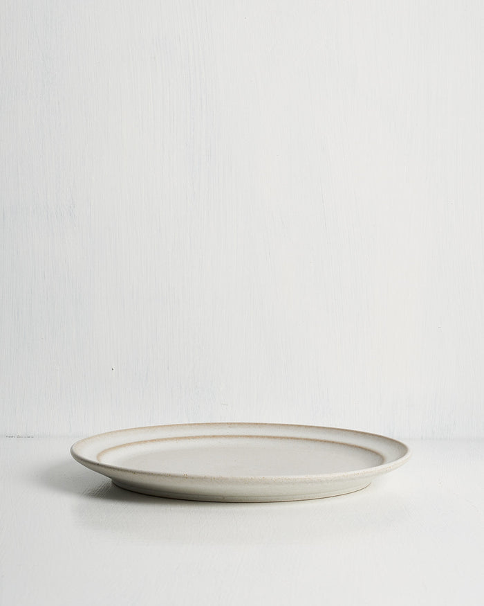 White ceramic pillar salad plate with a thin brown rim on a light gray background
