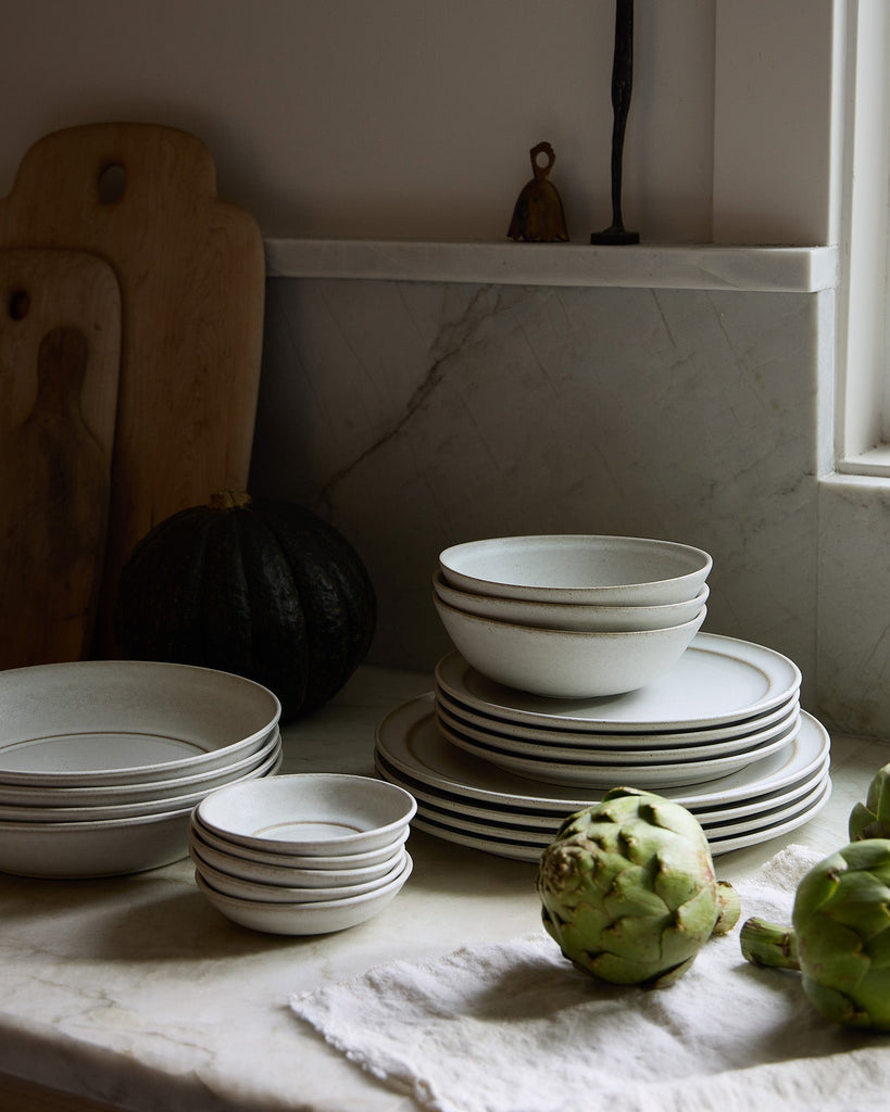 Stacks of white ceramic Pillar bowls and plates on a marble surface with a pumpkin and artichokes.