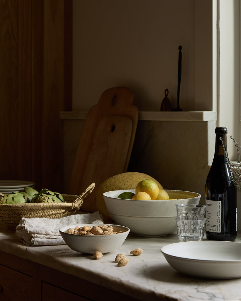 Dishes and food in Pillar Ceramic dishes on a counter with a bottle of wine in a dimly lit room.