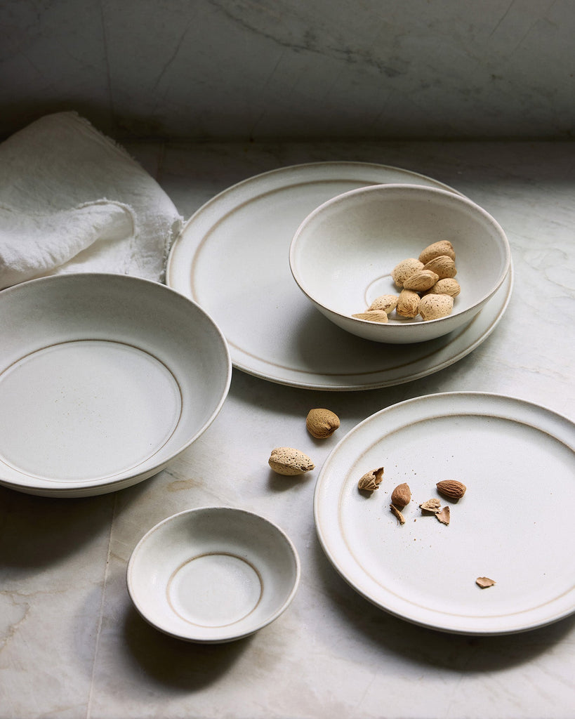 Set of ceramic Pillar plates and bowls on a stone surface with scattered nuts.