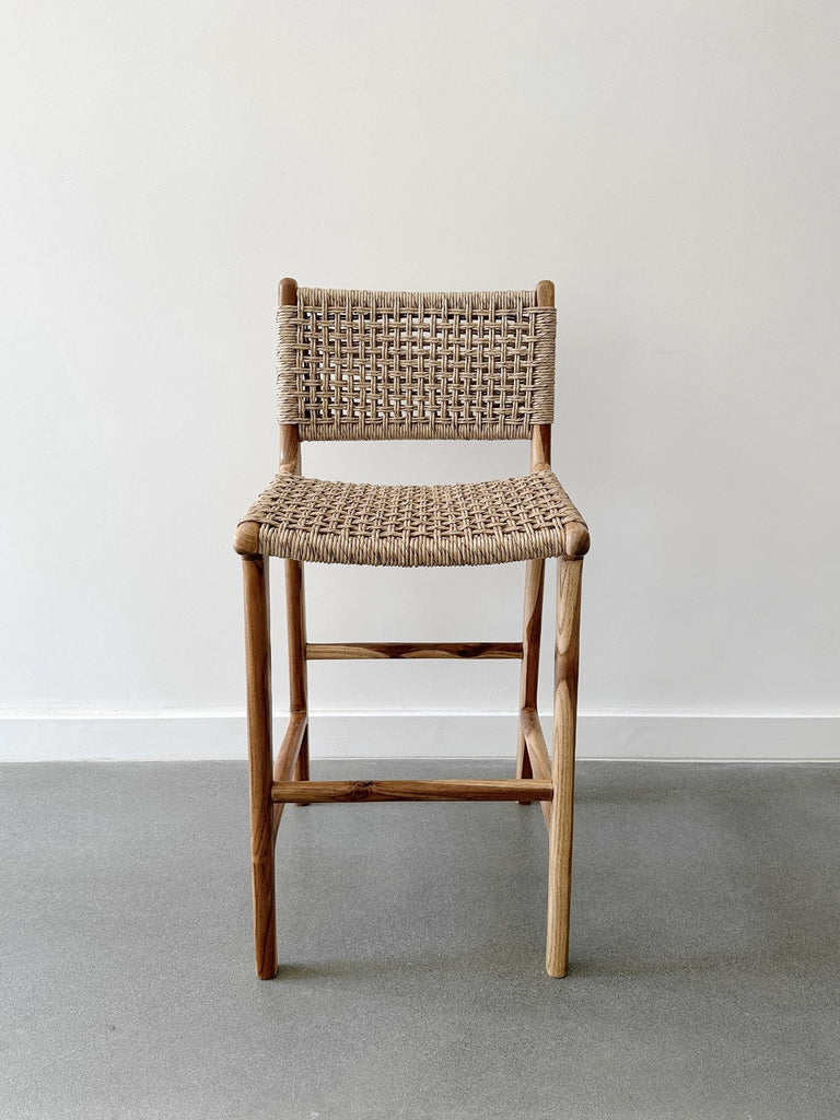 Front product view of the Faux Rattan Outdoor Counter Stool on concrete flooring and a white wall backdrop. - Saffron and Poe