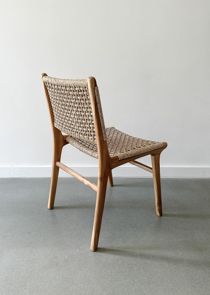 Back side product view of the Marin Woven Faux Rattan Indoor/Outdoor Dining Chair on concrete flooring and a white wall backdrop. - Saffron and Poe