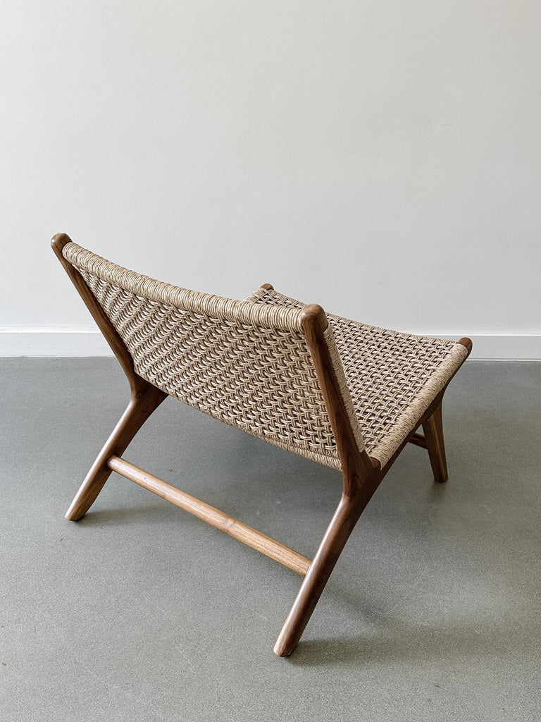 Back product view of the Woven Faux Rattan Marin Lounge Chair on concrete Flooring with a white wall backdrop. - Saffron and Poe