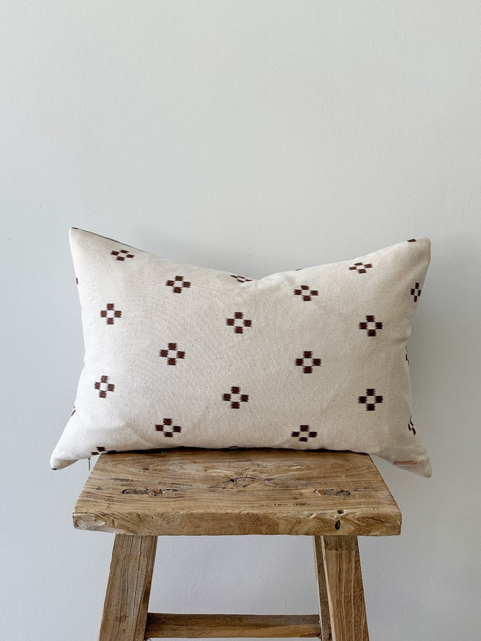 Front product view of the Brown Checkered Lumbar Pillow on a vintage stool with a white wall backdrop. -Saffron and Poe