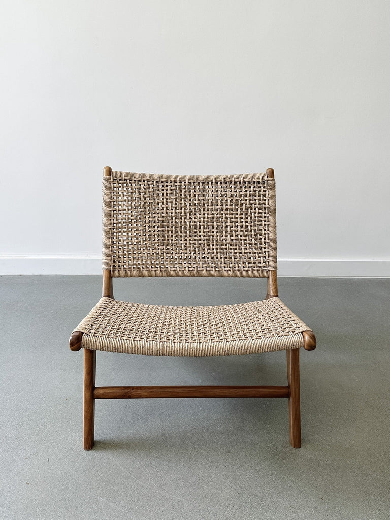 Front product view of the Woven Faux Rattan Marin Lounge Chair on concrete Flooring with a white wall backdrop. - Saffron and Poe