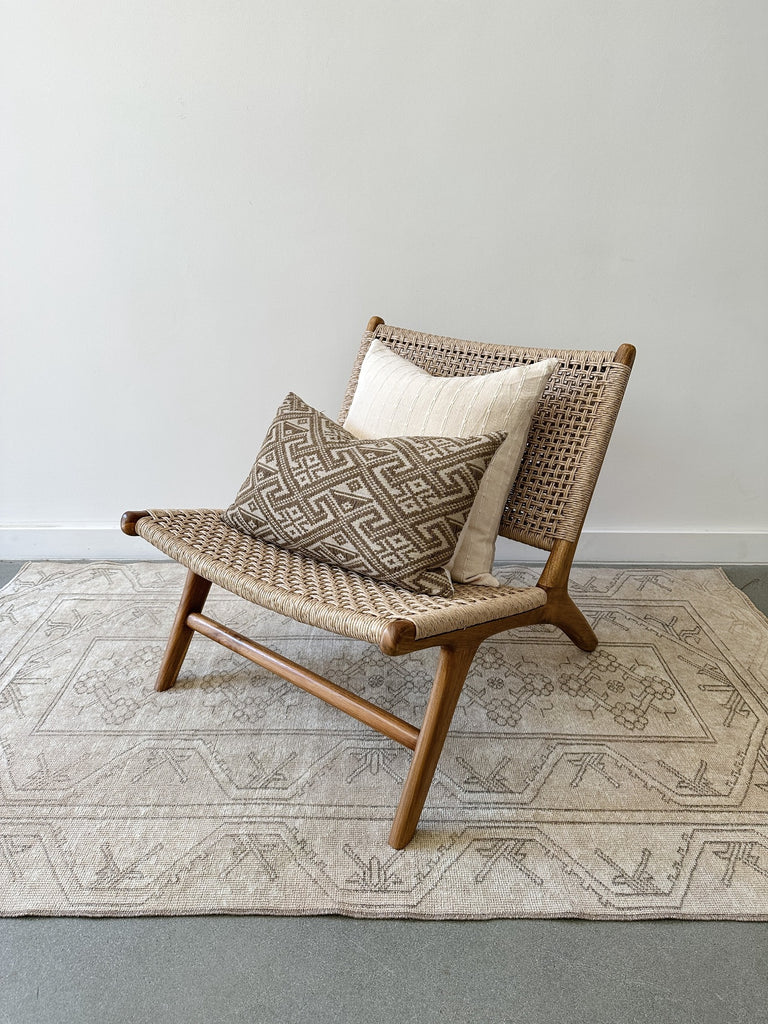 Side styled product view of the Woven Faux Rattan Marin Lounge Chair on concrete Flooring with a white wall backdrop. - Saffron and Poe