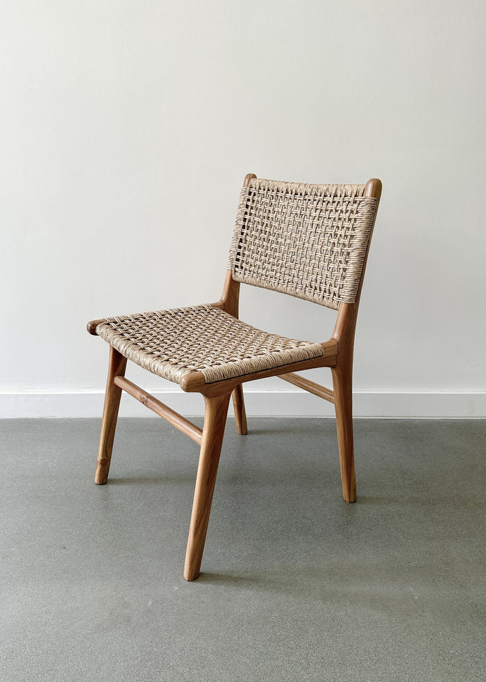 Side product view of the Marin Woven Faux Rattan Indoor/Outdoor Dining Chair on concrete flooring and a white wall backdrop. - Saffron and Poe
