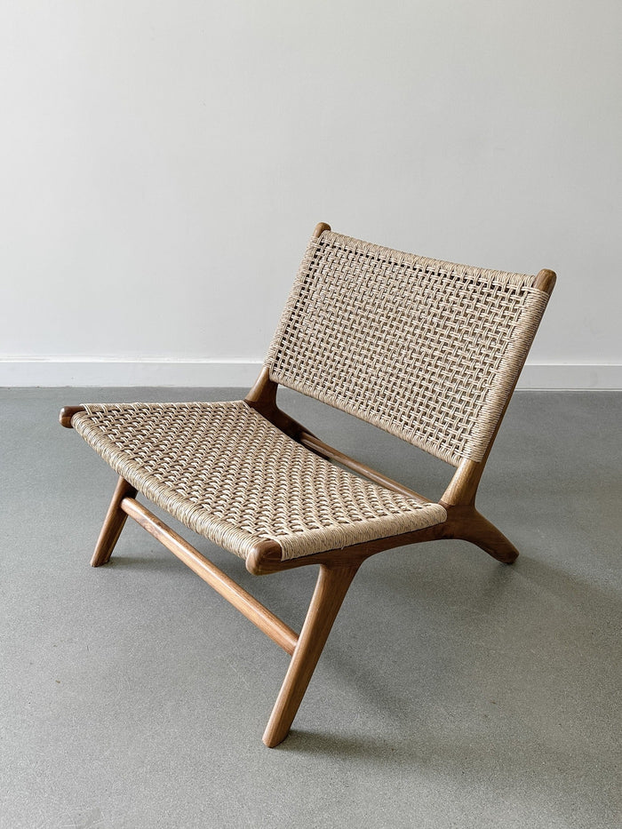 Side product view of the Woven Faux Rattan Marin Lounge Chair on concrete Flooring with a white wall backdrop. - Saffron and Poe