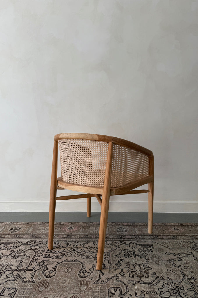 Wooden chair with wicker backrest on a patterned rug against a plain wall
