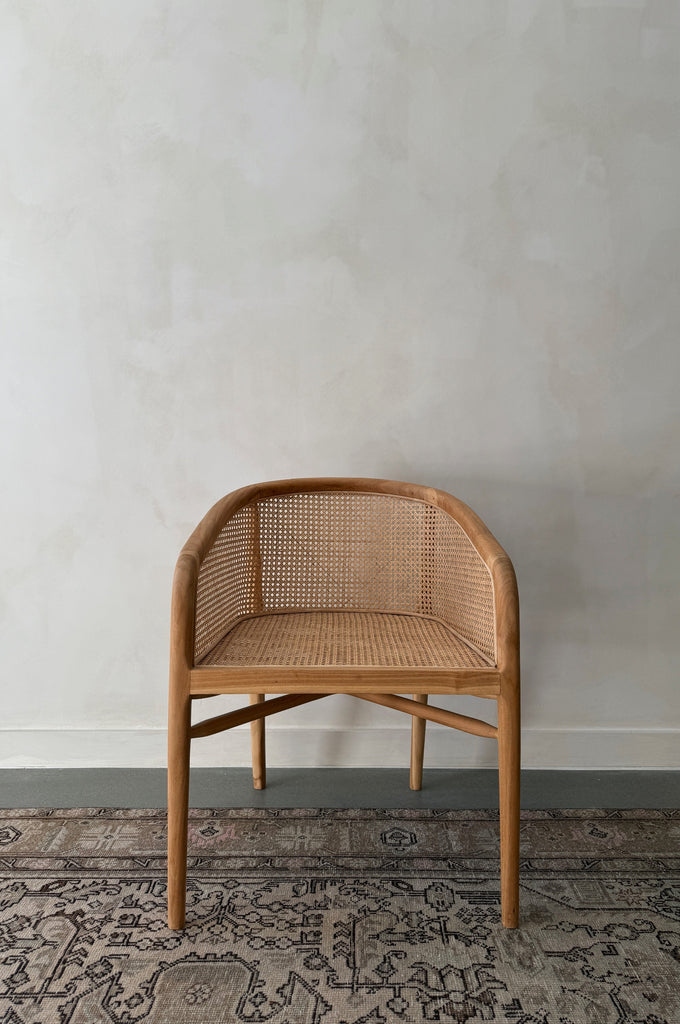Wicker chair against a plain wall with a patterned rug at the bottom.